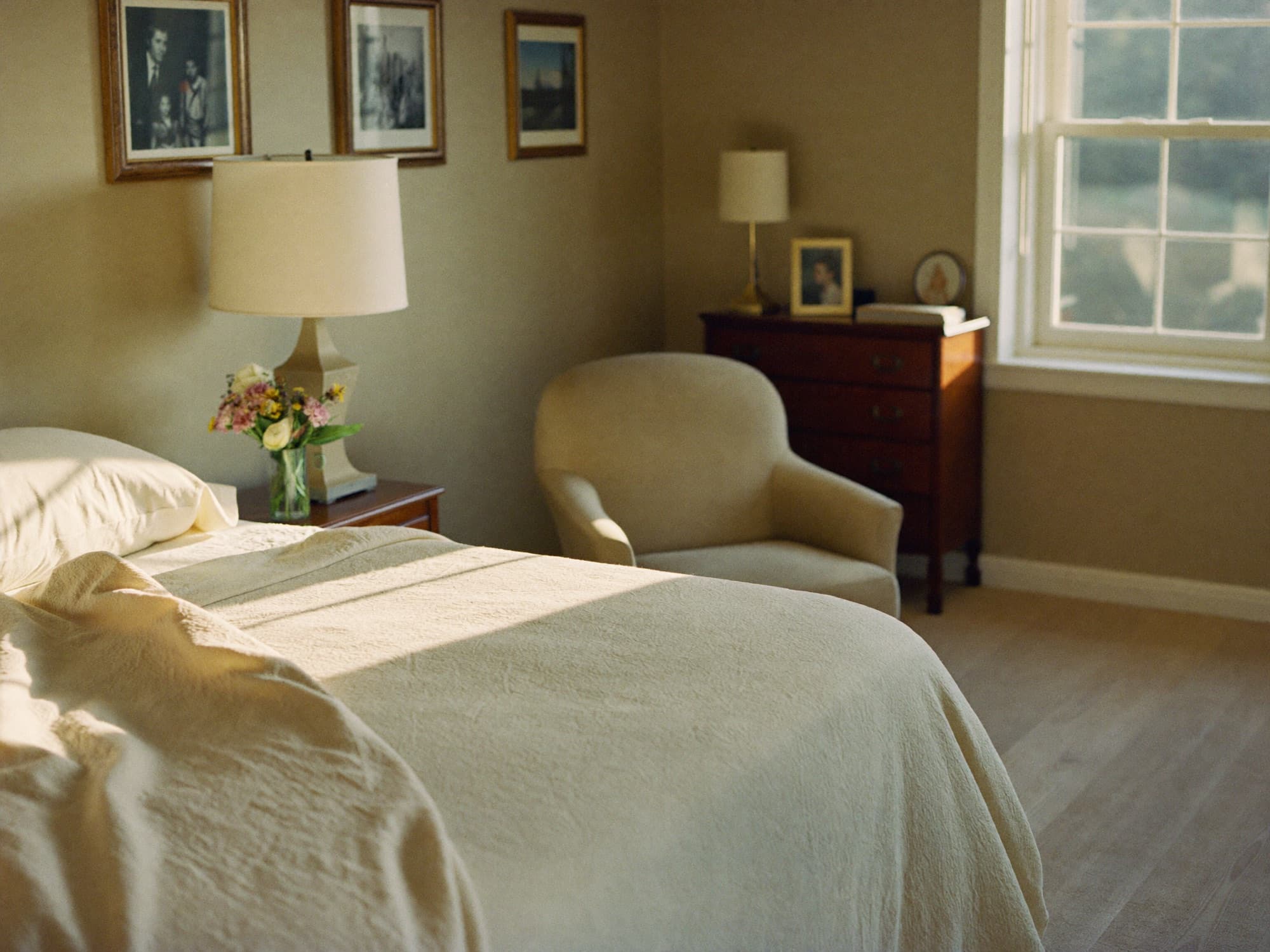 A bright, tidy private bedroom with soft cream linens and family photos