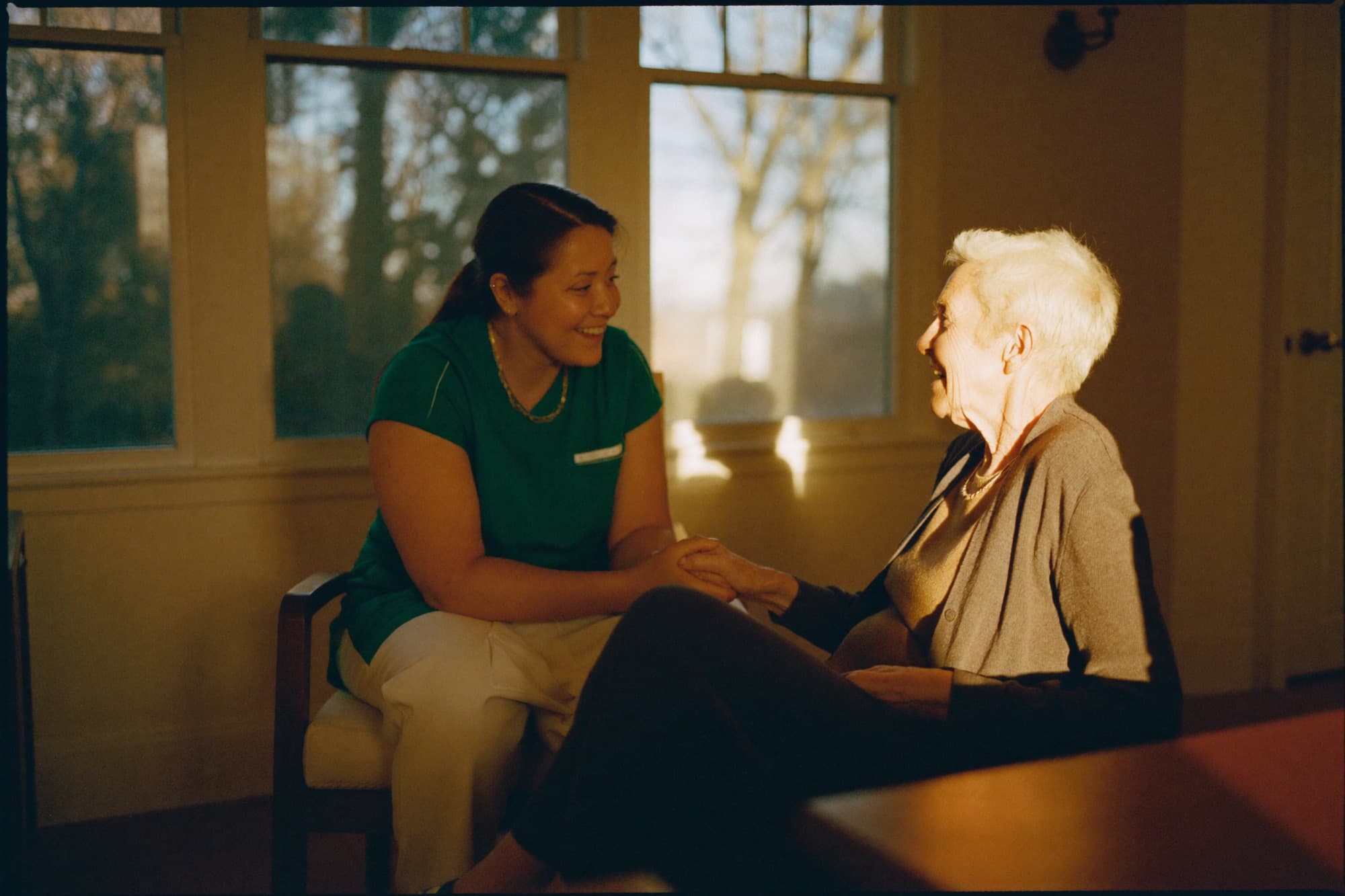 A caregiver gently holding a resident's hand in the care home — warm and reassuring