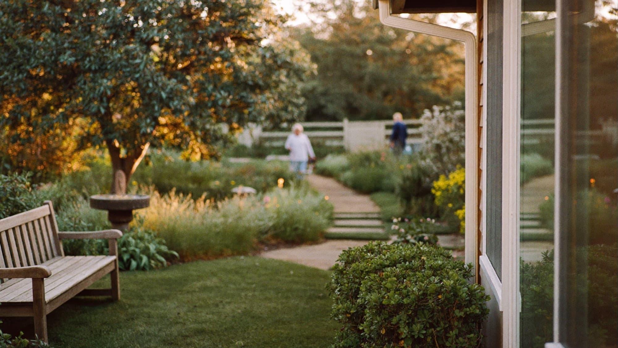 A peaceful enclosed garden path winding through flower beds in warm light at Valrico Family Care Home